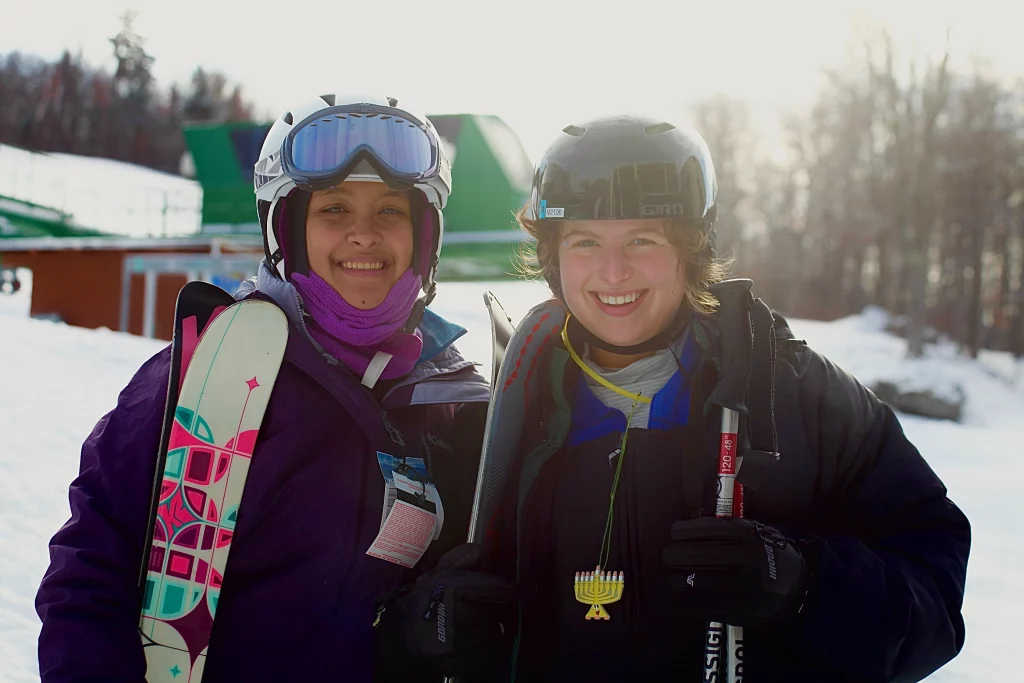 Students skiing together. Menorah is visible on necklace hanging from student on the right's jacker.