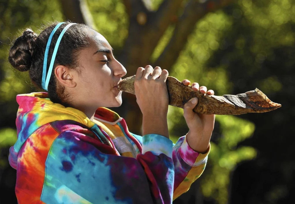 Student wearing a tie dyed sweatshirt blowing a shofar in celebration of Rosh Hashanah