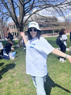 Student standing outside and smiling. She's at an Israel Independence Day celebration and is wearing a bucket hat and a white t-shirt