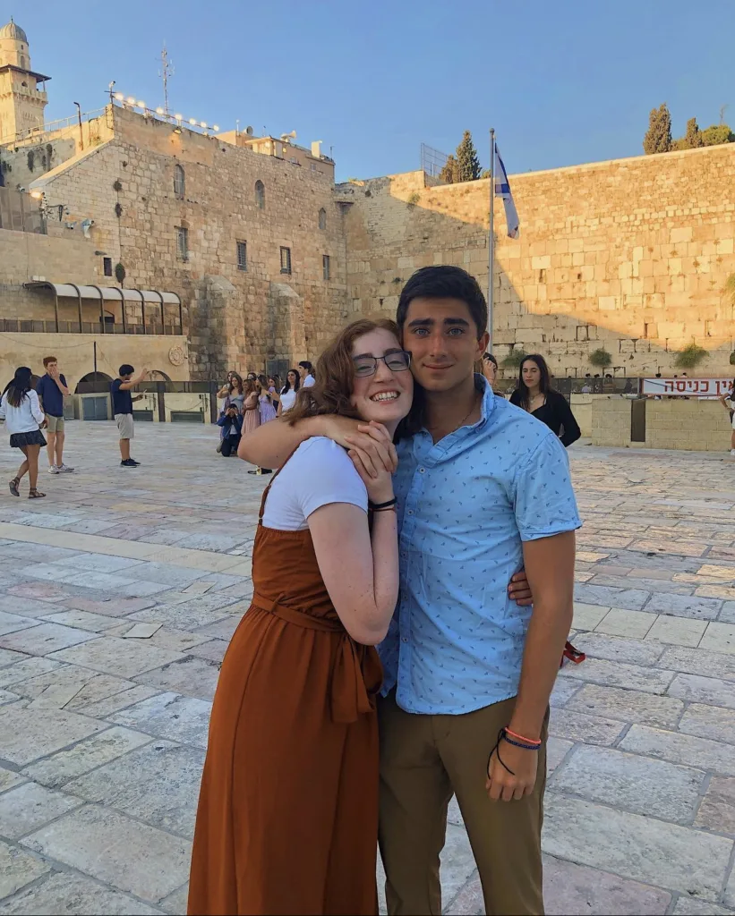 Two teenagers stand in front of the Western Wall in Israel. The author of this story is on the right in a blue button down shirt. 