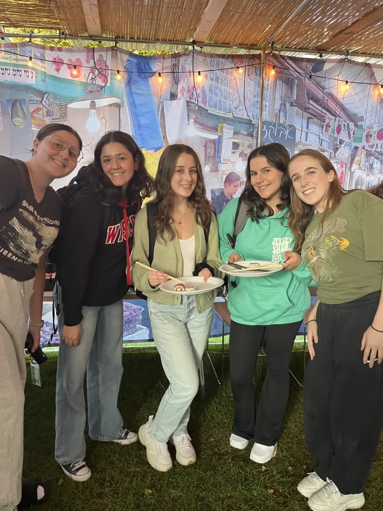 Students pose with plates of sushi in a sukkah.