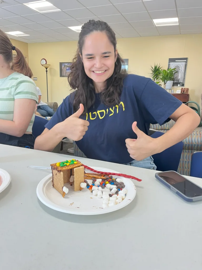 A student poses with their thumbs up behind a sukkah made of candy.